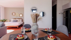 A modern hotel room with a bed, a dining table with two plates of fruit-topped pastries, a vase with dried plants, and wall-mounted mirrors. - Tribu Chapultepec 67 (Guadalajara)