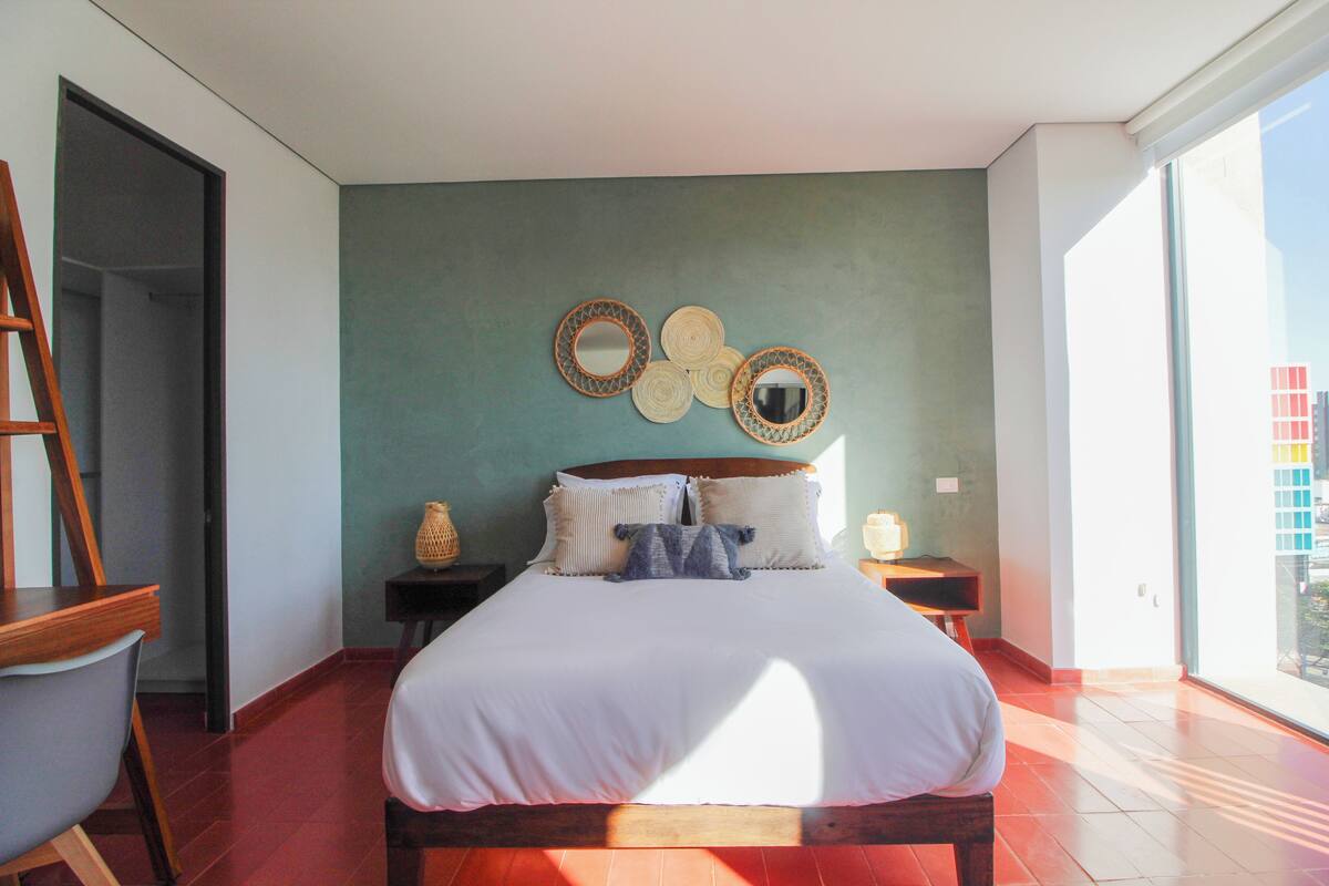Un dormitorio con cama, una escalera de madera, una mesita y un espejo fijado a la pared.