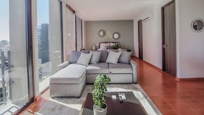 A modern living room with a sectional sofa, a coffee table with a plant, and a large window offering a city view. - Tribu Chapultepec 67 (Guadalajara)