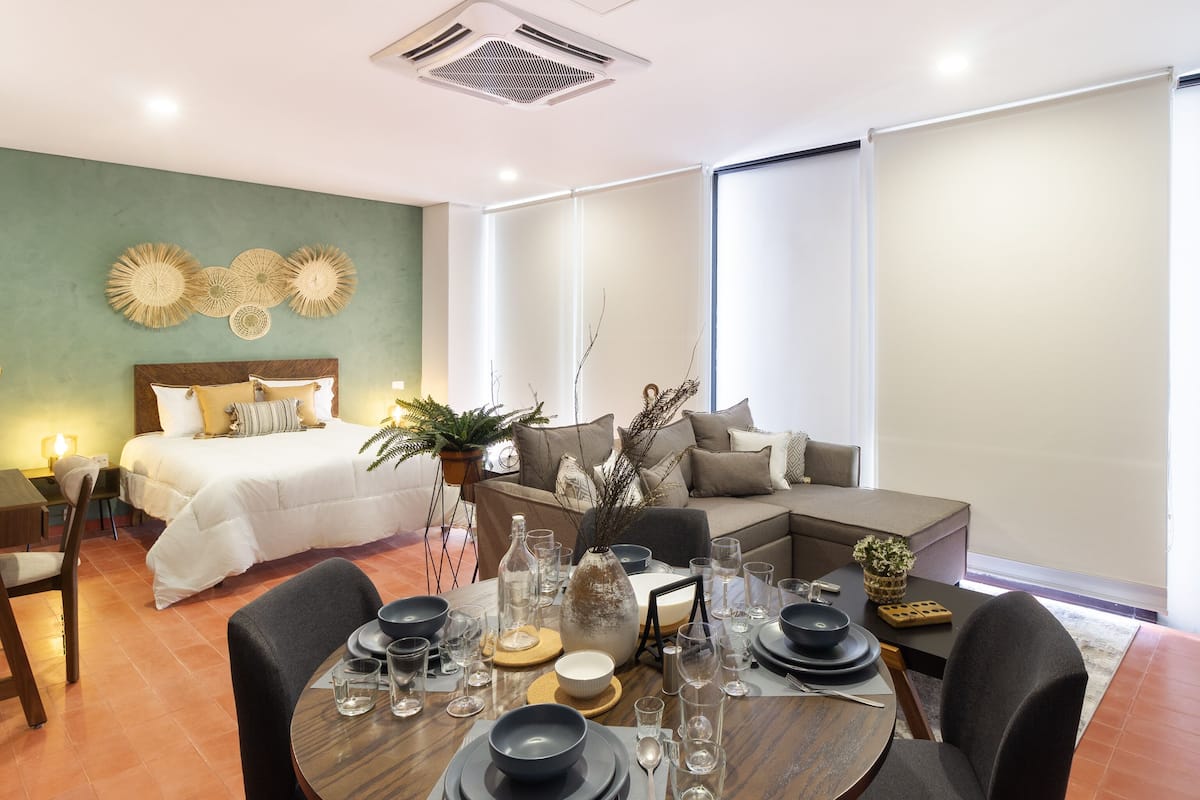 Habitación de hotel moderna con comedor para cuatro, cama con cabecero, sofá y ventana grande.