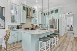 Una cocina moderna con armarios azul claro, una isla central con taburetes, un refrigerador de acero inoxidable y un microondas empotrado.