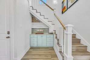 Un pasillo con una escalera, una zona de cocina con armarios azul claro y suelo de madera.