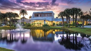 Un hotel con un estanque reflectante, palmeras y un cielo al atardecer.
