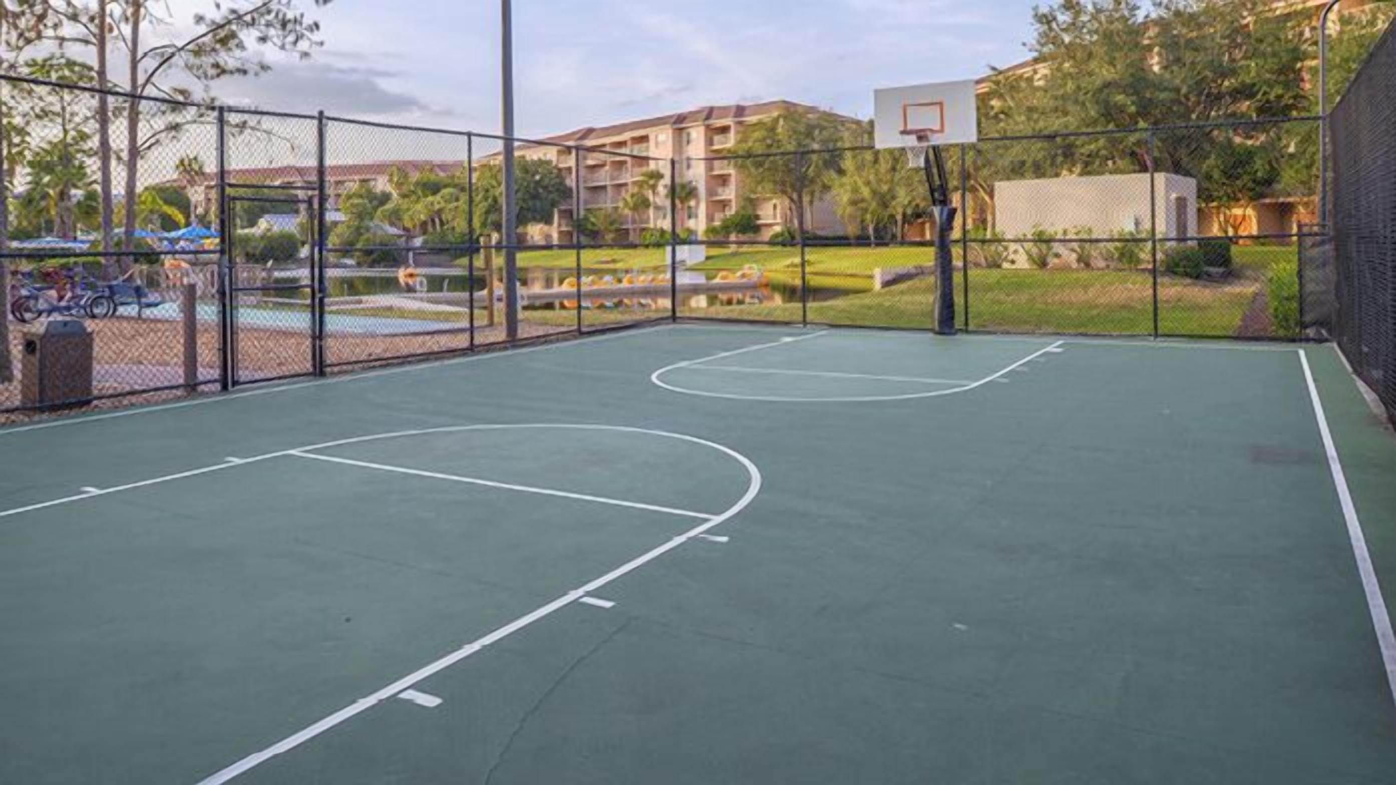 Una cancha de baloncesto al aire libre con valla, aro y un edificio en el fondo.