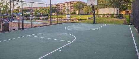 Una cancha de baloncesto al aire libre con valla, aro y un edificio en el fondo.