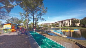 Ein Erholungsbereich mit einem Shuffleboard-Platz, einer kleinen Verkaufshütte und einem Gebäude im Hintergrund.