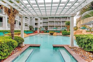 A pool area with a covered section, lounge chairs, and a building with balconies in the background. - Virginia Beach | Couples Ocean Coast Retreat | Pool + Hot Tub (Virginia Beach)