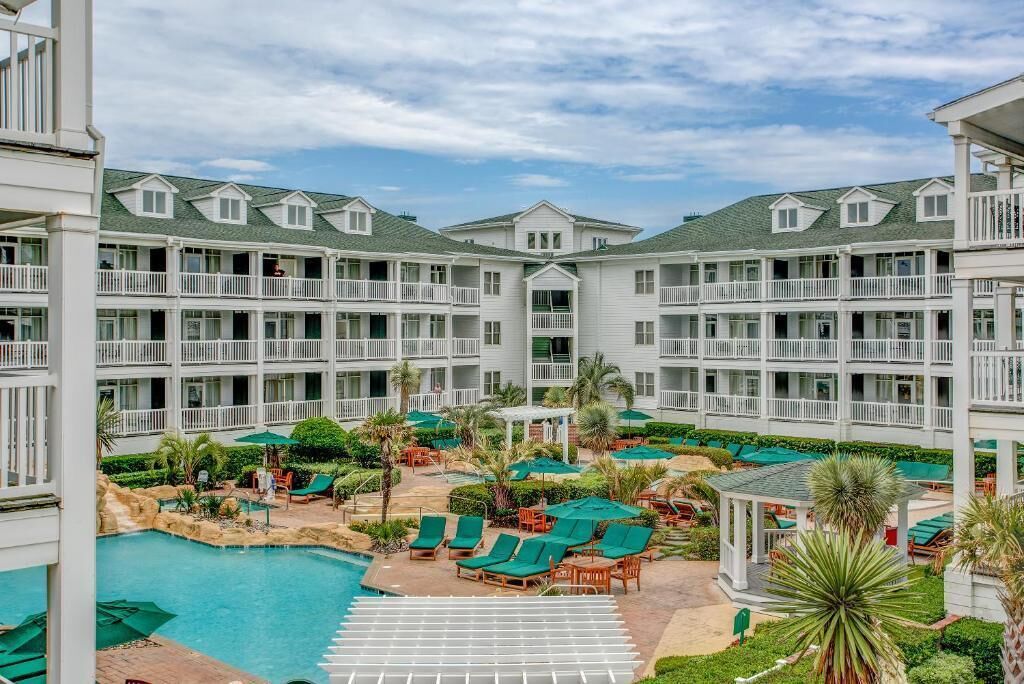Un hotel con zona de piscina, varios balcones y mobiliario exterior.