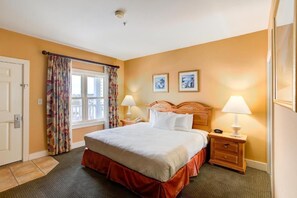 Une chambre d’hôtel avec un lit, deux tables de chevet avec des lampes, une porte et une fenêtre avec des rideaux.