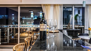 A bar area with a bottle of wine, two glasses, and a city view at night. - 2BR Family Apt Puente de la Mujer View (Buenos Aires)