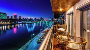 A balcony with wicker chairs and a table, overlooking a river with city lights and a bridge. - 2BR Family Apt Puente de la Mujer View (Buenos Aires)