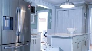 A kitchen with a stainless steel refrigerator, a white island with a bowl, and a hanging light fixture. - Riverside Getaway! Minutes to Downtown Woodstock (Woodstock)
