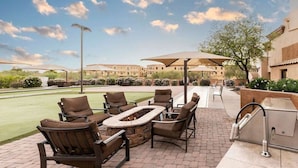 An outdoor patio area with a fire pit, seating, and a grill.