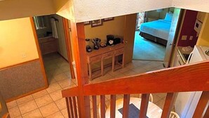 Una escalera que lleva a un dormitorio con una cama, una mesita con objetos y vistas al baño.
