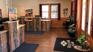 Un espace d’accueil avec des comptoirs de réception en bois, un paillasson et des plantes en pot.