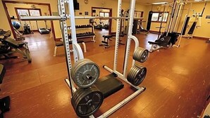 Une salle de sport équipée de matériel de musculation, de bancs et dotée d’un mur recouvert de miroirs.