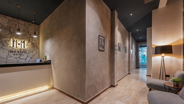 A hotel reception area with a stone wall, a reception desk, and a seating area with a lamp. - Hotel Mexico Merida (Mérida)