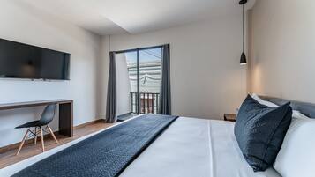 Habitación de hotel con cama, escritorio, silla, televisor, balcón y lámpara colgante.