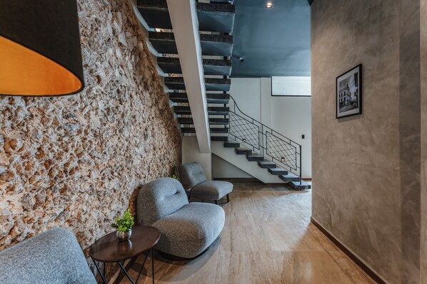 A modern interior with a stone wall, grey sofas, a staircase, and a framed picture on the wall. - Hotel Mexico Merida (Mérida)