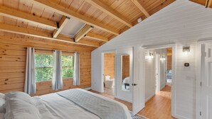 Quarto com uma cama grande, vigas de madeira no teto e vista para um banheiro por uma porta aberta.