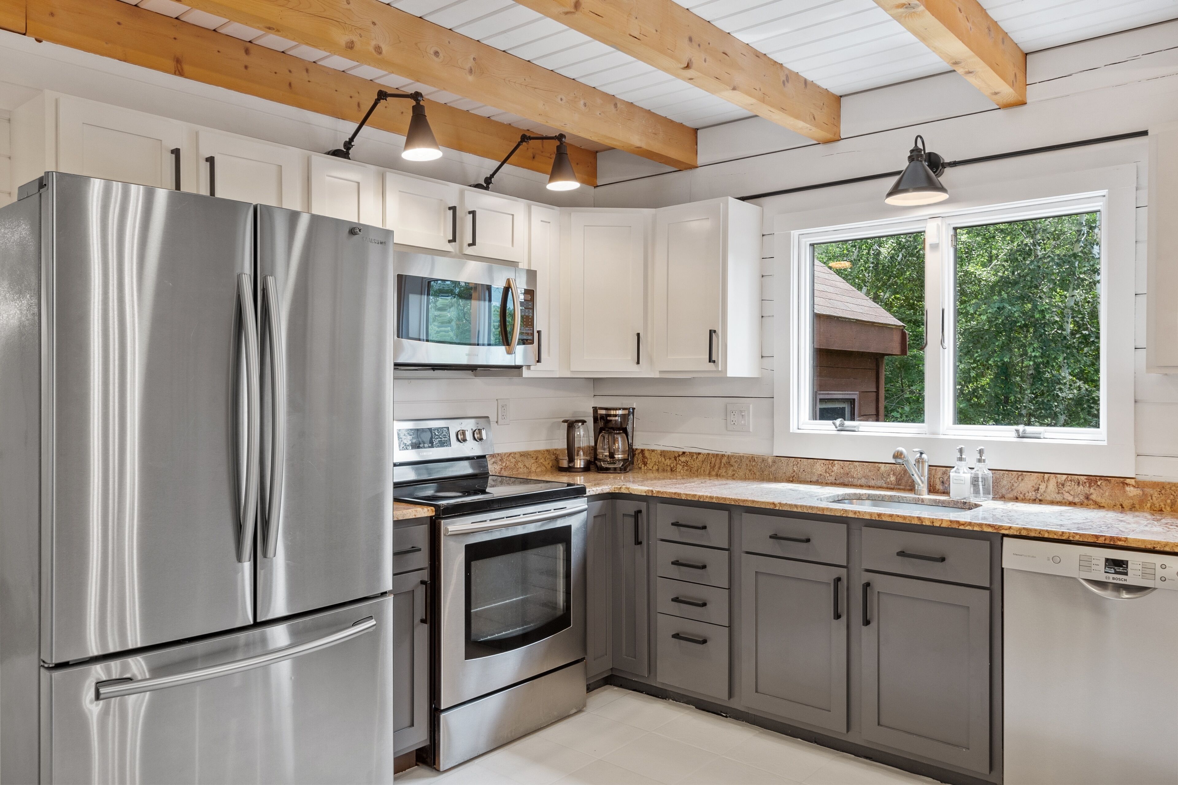 A modern kitchen with stainless steel appliances, white cabinets, and a window providing a view of greenery outside.
