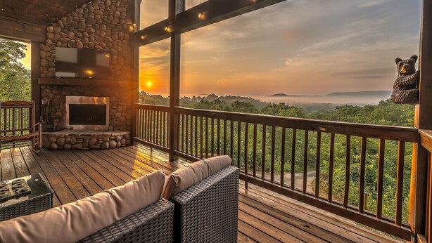 A wooden deck with a stone fireplace, wicker furniture, and a view of a forested landscape. - 10% Off Member Deal•OMG Views•10 Min to Downtown•Private•Hot Tub•Deck•Firepit (Blue Ridge)