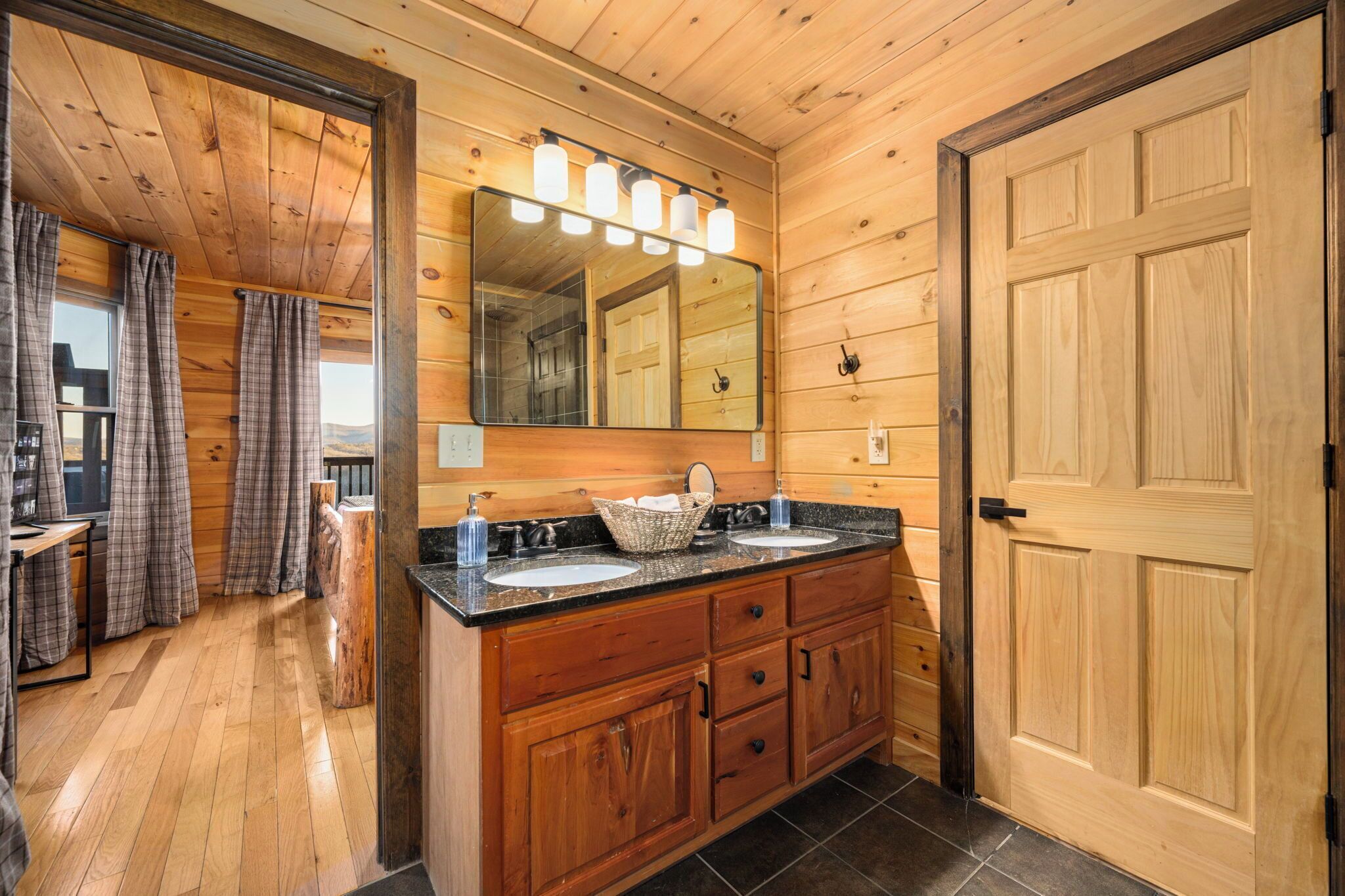 A wooden cabin bathroom with two sinks, a large mirror, and a wooden door.