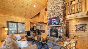 A cozy cabin interior with a stone fireplace, wooden walls, and a TV mounted on the wall. - 10% Off Member Deal•OMG Views•10 Min to Downtown•Private•Hot Tub•Deck•Firepit (Blue Ridge)