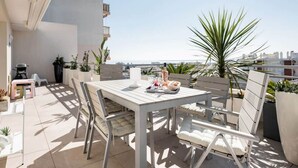 Un patio al aire libre con una mesa y sillas, plantas en macetas y vista al mar.