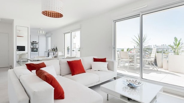 A modern living room with a white sofa, red cushions, and a large window offering a view of the outdoors. - Stroll to Beach from Sea-View Penthouse with AC (Antibes)