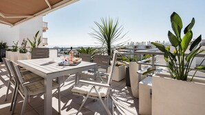 Terraza exterior con mesa y sillas, plantas en macetas y vistas al horizonte de la ciudad.