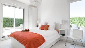 Un dormitorio moderno con una cama grande, vistas a zonas verdes y una silla blanca.