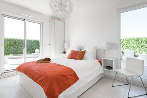 Una camera da letto moderna con un letto grande, vista sul verde e una sedia bianca.