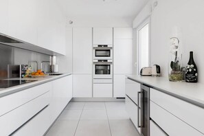 A modern kitchen with white cabinetry, a built-in oven, and a countertop with a toaster and a vase of flowers. - Stroll to Beach from Sea-View Penthouse with AC (Antibes)