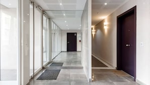 A modern hallway with glass doors, a dark door at the end, and a metal vent on the ceiling. - Stroll to Beach from Sea-View Penthouse with AC (Antibes)