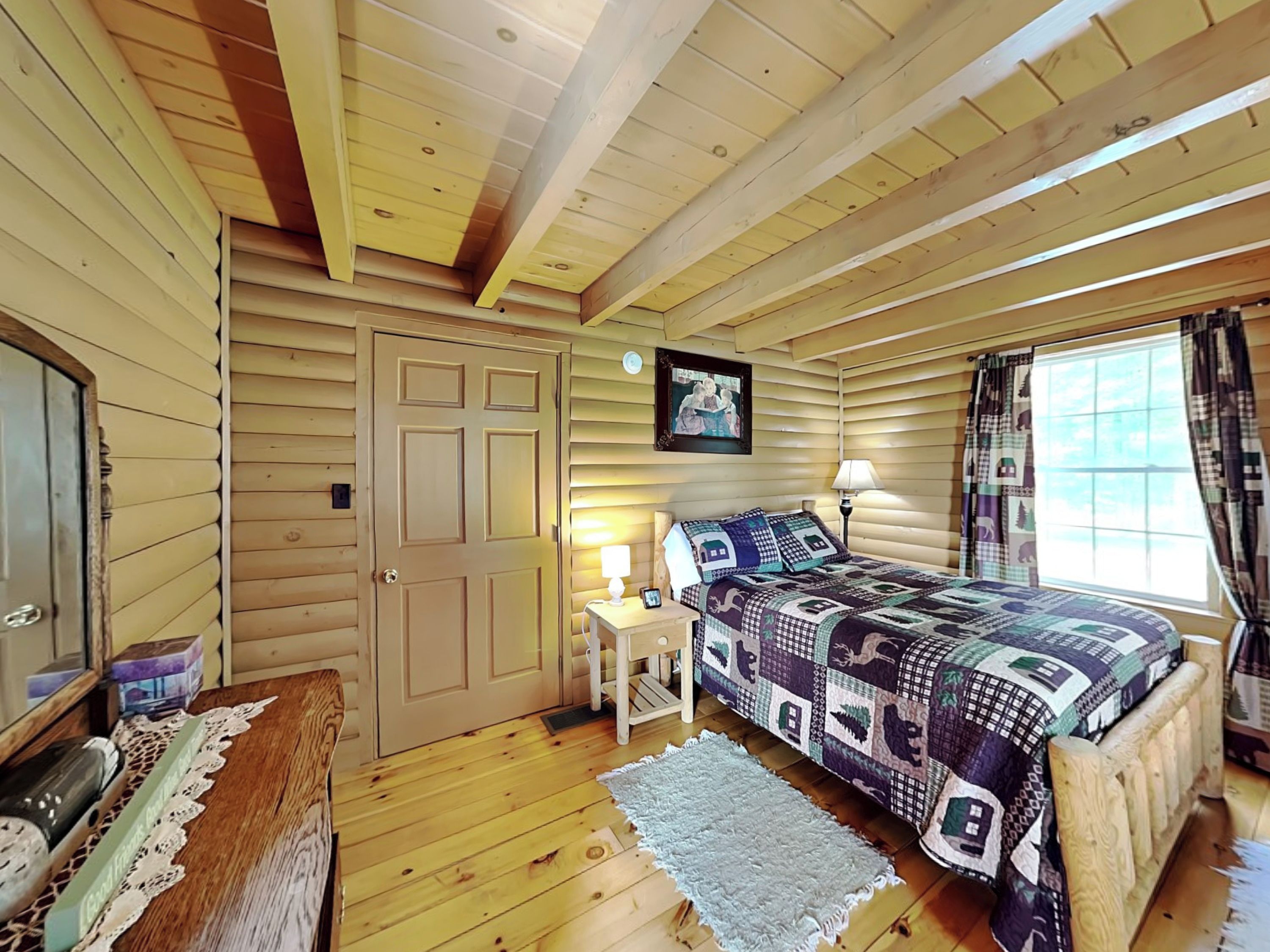 Un dormitorio acogedor estilo cabaña con paredes y techo de madera, una cama con colcha, una mesita de noche con lámpara y una ventana con cortinas.