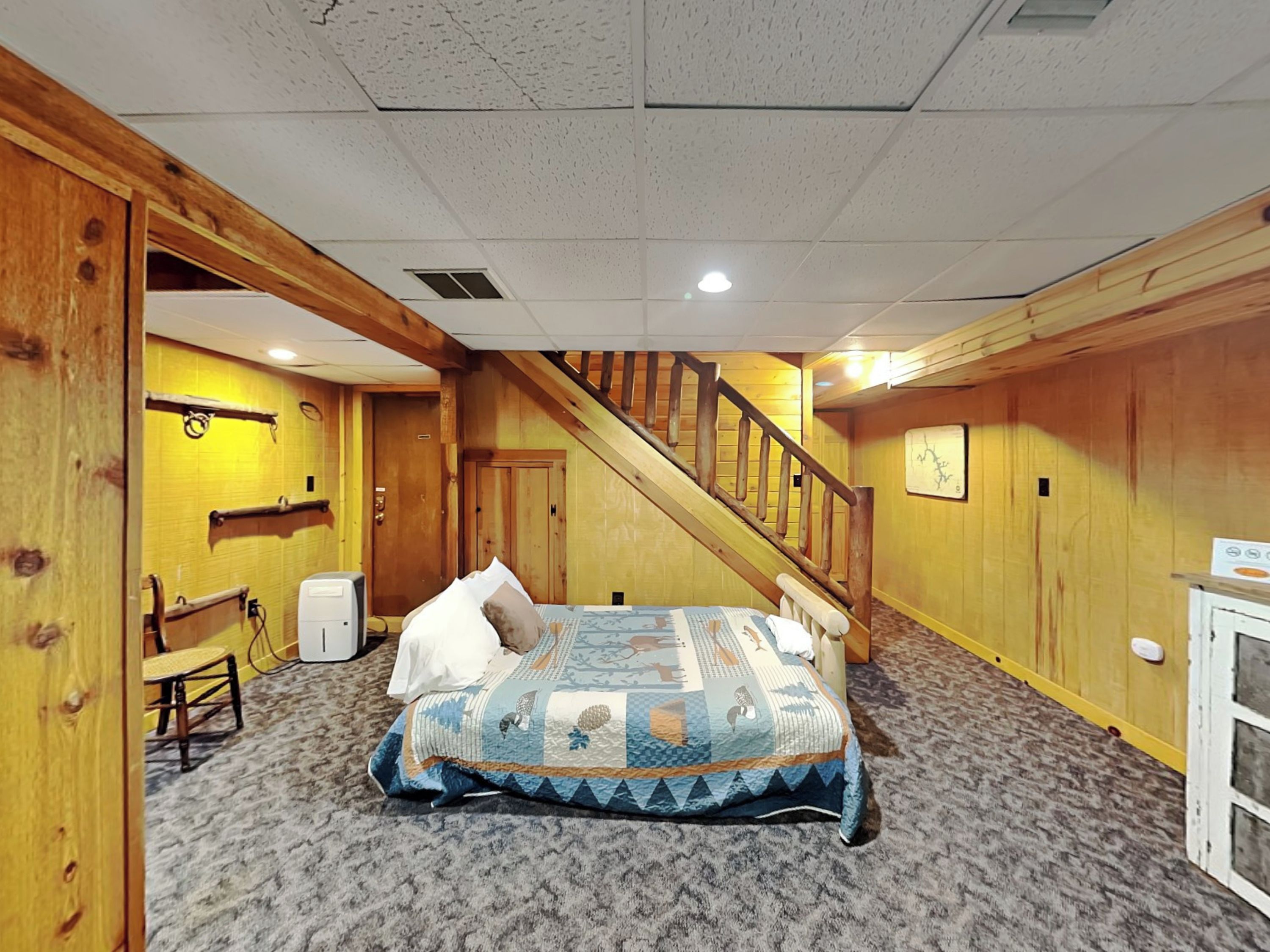 A bedroom with a wooden staircase, a bed with a quilt, a small table, and a chair.