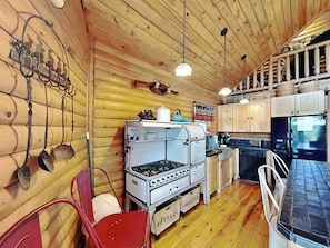Una cocina rústica con paredes de madera, una estufa a gas, armarios y un refrigerador.