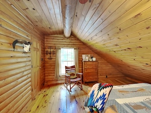 Un dormitorio acogedor en el ático con paredes de madera, techo inclinado, una mecedora, una cama con manta estampada y una decoración rústica que incluye un cráneo y una cruz.