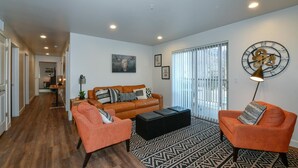 A modern living room with a brown leather sofa, two orange woven chairs, a black ottoman, and a patterned rug. - 2-E The Copper Ridge Condo (Moab)