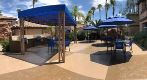 An outdoor patio area with covered seating, a barbecue grill, and palm trees in the background.