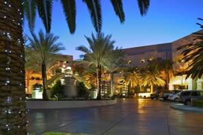 A hotel courtyard with palm trees, a pool, and a building with multiple floors and balconies.
