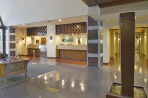 Un hall de hotel con mostrador de recepción, una barrera de cuerda roja y una columna decorativa.