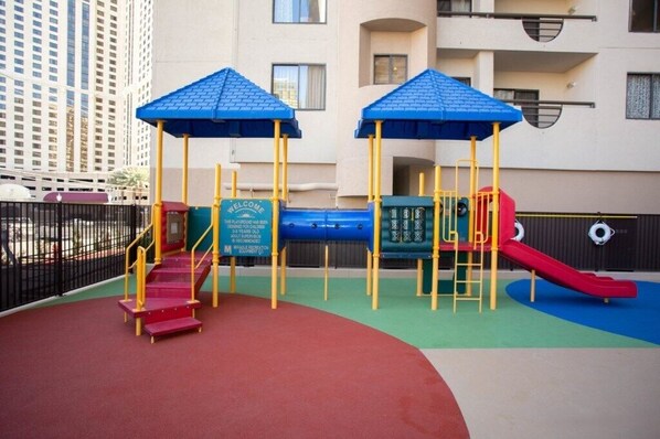 An outdoor playground with two blue-roofed play structures, a red slide, and a red staircase.
