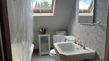 A bathroom with a bathtub, toilet, and sink. There is a small cabinet with a glass door and a window above the toilet.