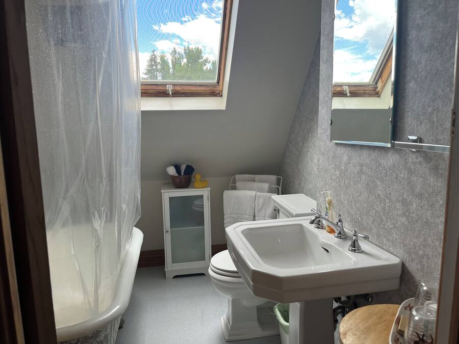 A bathroom with a bathtub, toilet, and sink. There is a small cabinet with a glass door and a window above the toilet.
