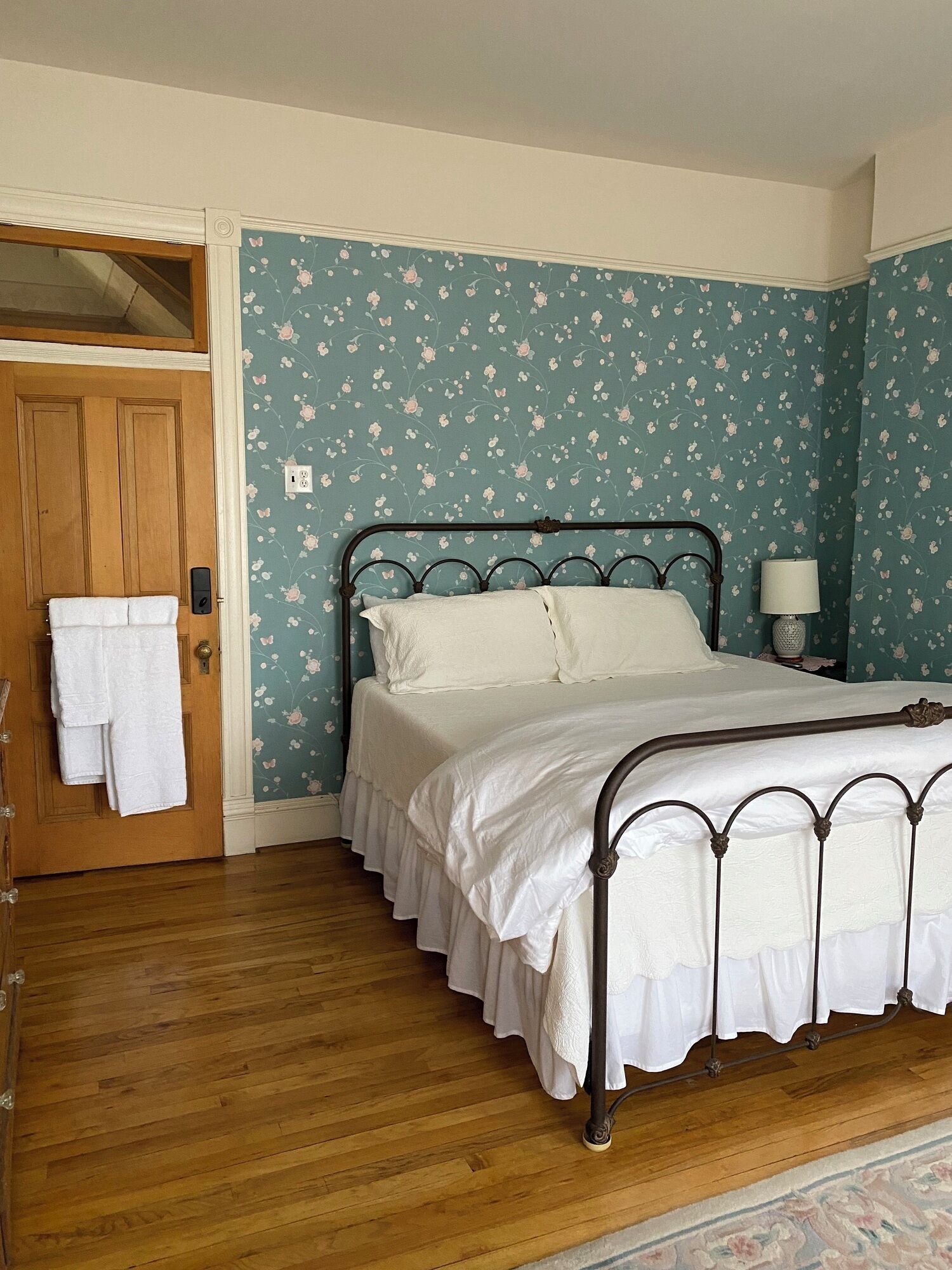 A bedroom with a bed, wooden door, and floral wallpaper.
