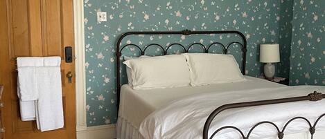 A bedroom with a bed, wooden door, and floral wallpaper.