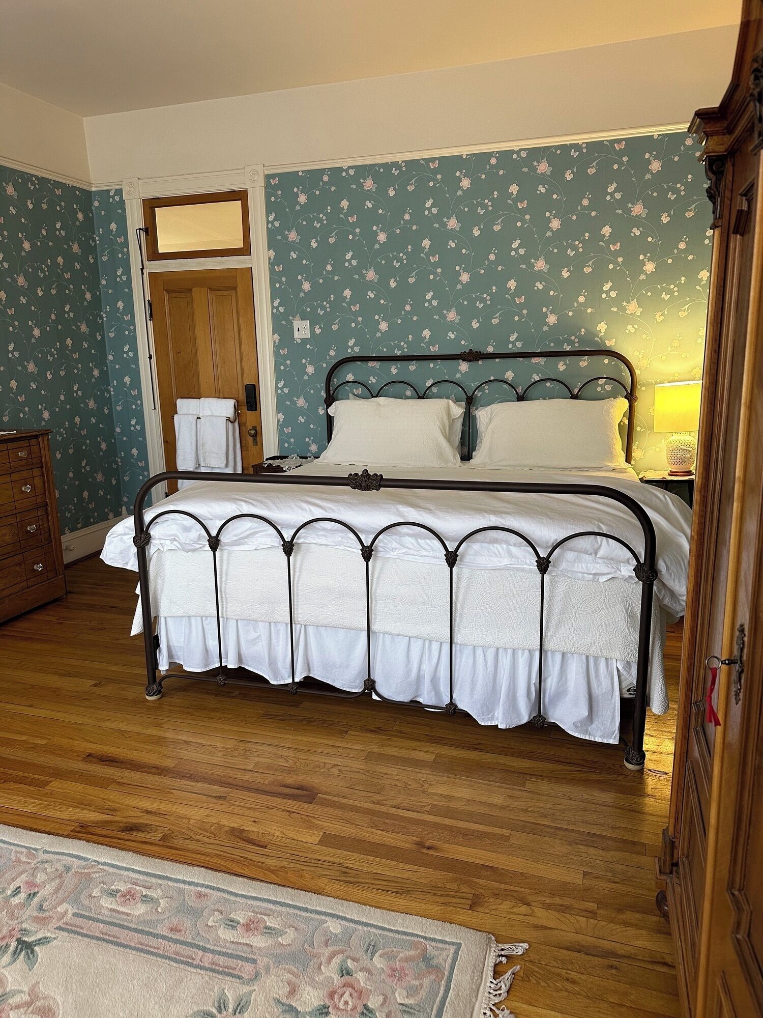 Ein Schlafzimmer mit Bett, Holzboden, Blumenwallpaper und einer Tür.