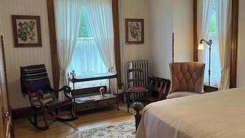 A bedroom with a bed, rocking chair, chair with a cushion, a small table, and a floor lamp.